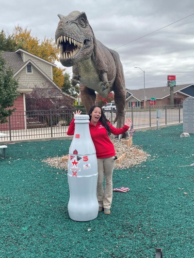 Kelly Clark, Route Sales Manager, “escapes” from a life-size T-Rex at Dinosaur Park in Woodward, Oklahoma with the Recognition Roadtrip Bottle on Oct. 28, 2021.