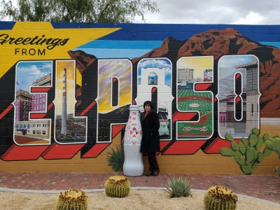 Laura Aragon, wife of Lalo Aragon – a ASMM at El Paso, poses with the Recognition Roadtrip Bottle in front of the iconic “Greeting from El Paso” mural on Nov. 26, 2021. This is just one of more than 100 vivid El Paso art murals found across the town that reflect the rich Mexican storytelling tradition of El Paso and its community pride.