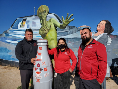 The Roswell team with the Recognition Roadtrip Bottle in front of the “Welcome to Roswell” artwork on Dec. 7, 2021. Created by John Cerney, this cut-out artwork depicts a family welcoming larger-than-life aliens.