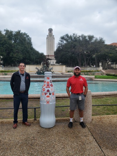 Chris Villasenor, ORM Lead Small Store, and Jeremiah Dawson, ORM Lead Small Store, with the Recognition Roadtrip Bottle in front of UT Tower on Dec. 30, 2021. Located in downtown Austin, the 307-foot-tall building is at the center of the University of Texas’ campus.