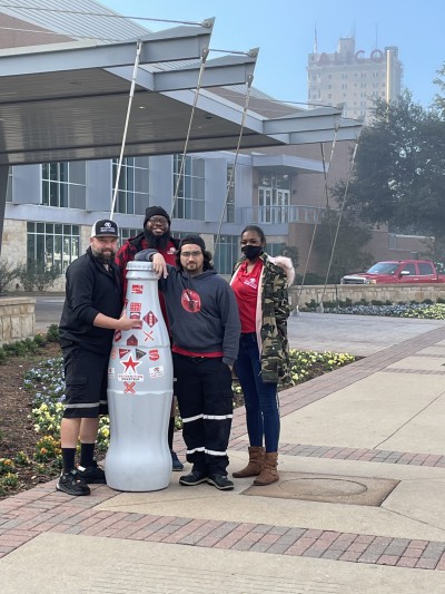 Waco heroes with the Recognition Roadtrip Bottle outside the Waco Convention Center with the Alico building in the background. The Alico building is currently the tallest building in Waco with a height of 282 feet.