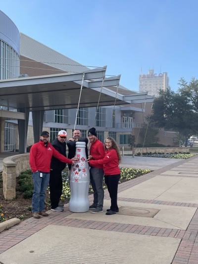 Waco heroes with the Recognition Roadtrip Bottle outside the Waco Convention Center on Dec. 21, 2021. The city’s iconic Alico building can be seen in the background.
