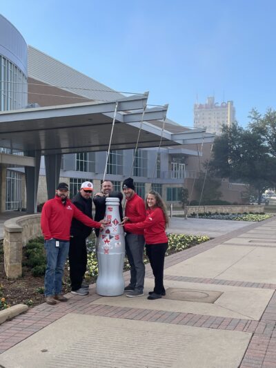 Waco heroes with the Recognition Roadtrip Bottle outside the Waco Convention Center on Dec. 21, 2021. The city’s iconic Alico building can be seen in the background.