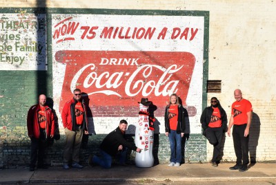 Paris heroes pose with the Recognition Roadtrip Bottle in front of the Coca-Cola mural at the Lamar Theater on Feb. 15, 2022. Located in downtown Paris, the Lamar Theater was built in 1929 and closed in 1963. After its closing, sheet metal was added to the building, hiding the theater for over half a century. But during renovations in 2018, contractors removed the metal to reveal the old brick theater still intact – complete with this vintage Coca-Cola mural painted on the side!