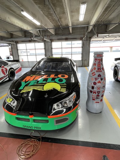 The Recognition Roadtrip Bottle meets the Mello Yello car in the garage at Texas Motor Speedway on March 22, 2022. Coca-Cola brands are popular at the races…each year, people drink enough Coca-Cola, Dasani water, coffee and hot chocolate to fill the 34,000-gallon Texas-shaped pool at the Lone Star Tower Clubhouse on the TMS property.