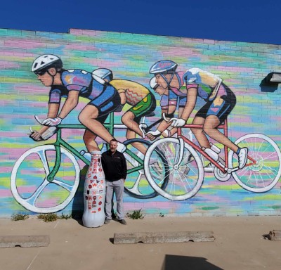 Wichita Falls hero, Jerry Cantwell, Sales Execution Manager, and the Recognition Roadtrip Bottle stop by the Hotter ‘n Hell Hundred mural in downtown Wichita Falls on March 28, 2022. The mural, one of 11 murals across Wichita Falls painted by artist Ralph Stearns, represents bicyclists riding in the city’s annual 100-mile bike ride.