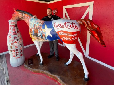 Giddy up! Wichita Falls hero, Adam McCown, Warehouse Supervisor, introduces the Recognition Roadtrip Bottle to the Coca-Cola horse outside the Wichita Falls distribution facility on March 28, 2022. The painted horse is part of a city-wide public arts project called the Mane Event. Over 70 fiberglass horses painted by local artists all across the city have been sponsored by local businesses and organizations.